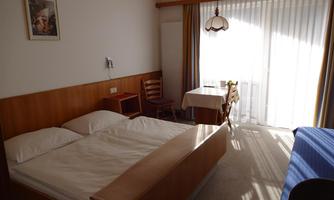 A simple room with a double bed and a table.  
Large windows let in plenty of light and provide access to the balcony.