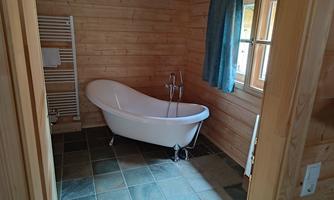 A stylish bathroom with a freestanding bathtub and wooden panels. A window with blue curtains lets in natural light.