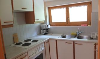 A bright kitchen with modern appliances and white furniture. Daylight falls on the countertop through the windows.