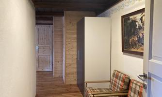 A corridor with wooden flooring and light-colored walls. On the left side, there is a coat rack and an upholstered chair.