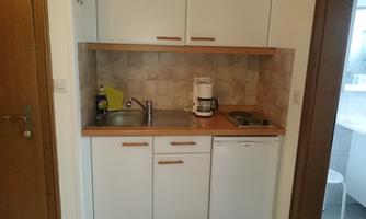 A small kitchen unit with a sink, a stove, and a refrigerator. The walls are bright and the wooden surfaces give a cozy impression.