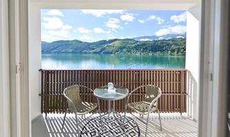 A beautiful balcony with a view of a tranquil lake and green hills. Two chairs and a table invite you to relax.