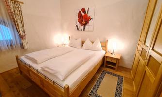 A cozy bedroom with a double bed and two nightstands. The walls are painted in neutral colors, featuring a decorative piece of artwork and warm lighting.