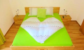 A cozy bedroom with a green bed and a heart-shaped towel arrangement. Next to the bed are two nightstands with lamps.