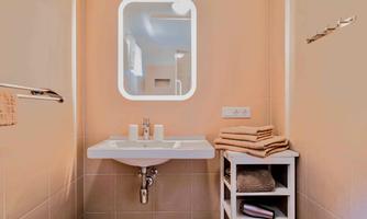 A modern bathroom with a white sink and a mirror. Towels and toiletries are neatly placed on a shelf.