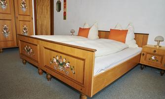A cozy bedroom with a large wooden double bed. The bedding is white, and the pillows are orange.