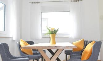 A bright dining area with a square table and modern chairs. A vase with fresh flowers is on the table.