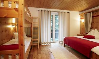 A cozy room with a bunk bed and a double bed. Large windows let in plenty of light and provide a view outside.