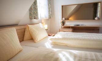 A bright bedroom with two cozy beds and soft pillows. A mirror and a small table complete the furnishings.