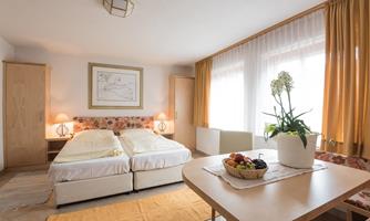 A cozy bedroom with two single beds and a large window. 

On the table, there is a fruit bowl and a plant creates a pleasant atmosphere.