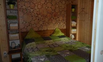 A cozy bedroom with a wooden wall design and a double bed. The bed linen is in various shades of green and patterns.