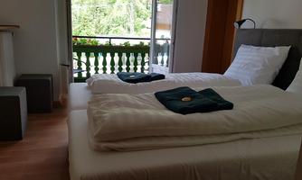 A modern bedroom with two beds and a cozy decor. The view of the balcony offers a green outlook to the outside.