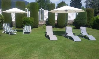 A beautiful garden with loungers and sun umbrellas. Lush grass and well-maintained hedges create a relaxing atmosphere.