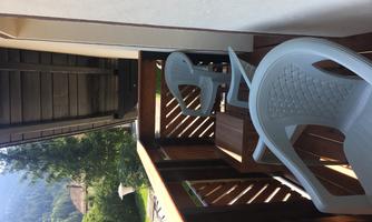 A balcony with two white plastic chairs and a view of nature. In the background, mountains and trees are visible.