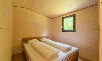 A simple bedroom with wooden paneling. There is a double bed and a window that lets in daylight.