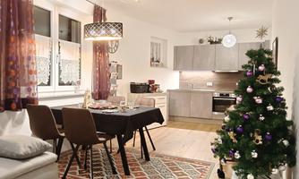 A cozy living space with a table and chairs, featuring a festive table decoration. In the corner stands a decorated Christmas tree.