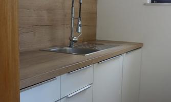 A modern kitchen with white cabinets and a wooden countertop. The faucet is elegant and the light comes through a window.