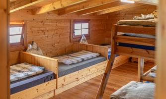 A cozy sleeping area with wooden furniture and several beds. The room has a warm atmosphere and large windows that let in natural light.