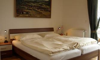 A cozy bedroom with a large bed and a painting on the wall. The room is bright and has a warm wooden floor.