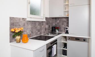 A modern kitchen with bright colors and elegant cabinets. On the countertop, there are flowers and a container with juice.