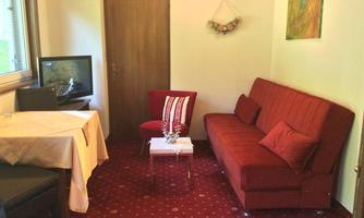 A cozy living room with a red sofa and a small table. A television is in the corner, and a window lets in plenty of daylight.