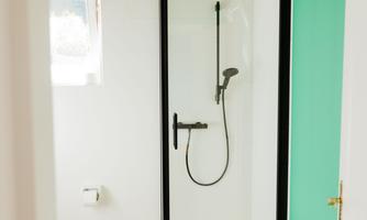 A modern bathroom with a shower cubicle and bright tiled floor. The wall is painted in a fresh green, providing a modern accent.