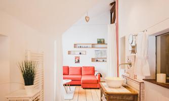 A bright room with a red sofa and a wooden floor. In the foreground, there is a sink on a wooden stand.