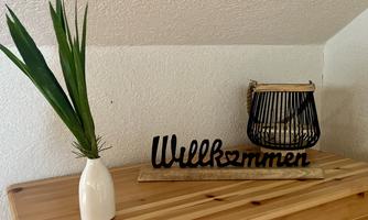 A stylish decoration with a welcome sign and a vase with a plant. In the background, there is a basket that complements the friendly atmosphere.