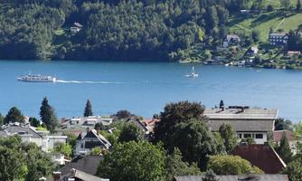 A beautiful view of a lake with two boats. In the background, green hills and a residential area can be seen.