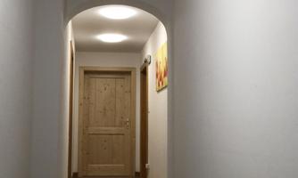 A bright hallway with a wooden door at the end. The walls are white and the floor is covered with a carpet.