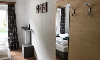 A cozy bedroom with two beds and a large mirror. White walls and dark curtains give the room an inviting atmosphere.