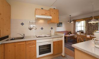 A cozy kitchen with wooden cabinets and modern appliances. In the background, there is a dining area with a table and chairs.