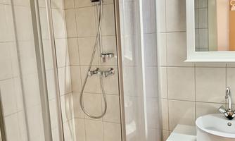 A modern bathroom with a shower cabin and a sink. The walls are tiled with light-colored tiles.