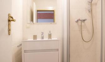 A modern bathroom with a shower, a sink, and a large mirror. The walls are light and tiled, and the floor is tiled.