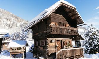 A charming wooden house in the winter snow, surrounded by snow-covered trees. The clear blue sky complements the idyllic scene.