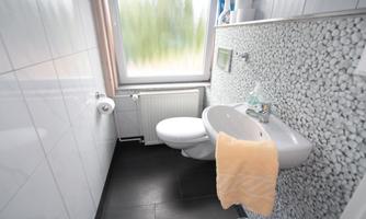 A modern bathroom with white tiles and stone décor. A toilet and a towel are visible, as well as a window with a view to the outside.