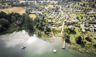 A picturesque campsite by the water with many RVs and green trees. The landscape is tranquil and welcoming.