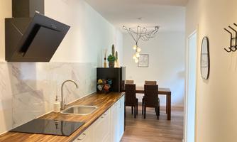 A modern kitchen with a wooden countertop and ceramic hob. In the background, there is a dining area with a table and chairs.