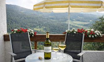 A beautiful balcony with a view of the mountains. On the table are a bottle of white wine and two glasses.