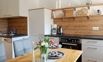 A modern kitchen with wooden details and bright cabinets. Fresh tulips are on the table along with a plate of small pastries.