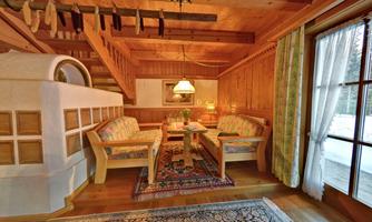 A cozy living area with wooden walls and a staircase in the background. Two sofas and a table are arranged in the center, surrounded by a carpet.