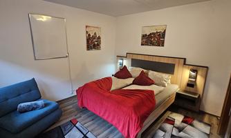 A cozy bedroom with a large bed and red pillows. Next to the bed is a blue couch and decorative pictures on the wall.