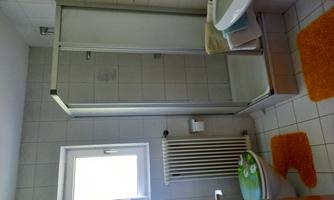 A small bathroom with a shower, a sink, and a toilet. The room has light tiles and orange bathroom mats.