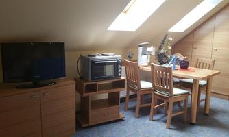 A cozy room in the attic with a table, chairs, and kitchen utensils. A television and a microwave complement the furnishings.