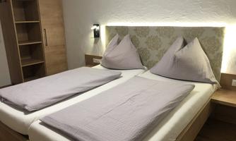 A cozy bedroom with two single beds and warm lighting. The walls are light-colored and the furniture is made of wood.