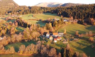 A picturesque landscape with gentle hills and forests. In the foreground, a small village can be seen, surrounded by green meadows.