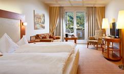 A cozy hotel room with two beds and a balcony. The decor is modern and inviting, with a small living area.