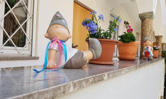 A decorative figure sits relaxed on a wall. Next to it are flowerpots with colorful flowers.