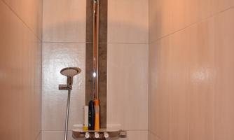 A modern shower with a large rain showerhead and an elegant design. The walls are made of light tiles.