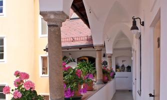 A quiet hallway with columns and colorful flowers. Light floods the space, creating an inviting atmosphere.